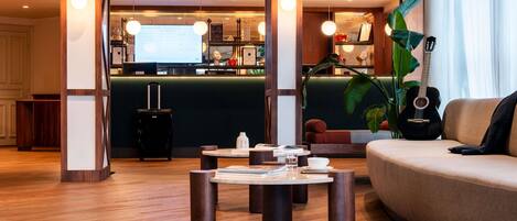 A modern hotel lobby with a reception desk, a seating area with a sofa and a coffee table, and a large plant.