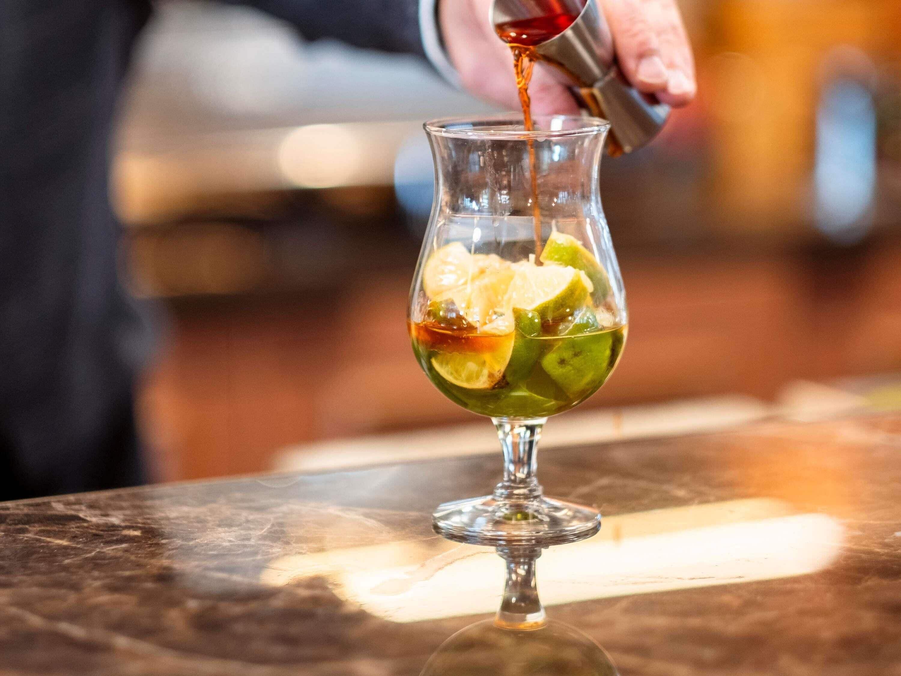 A cocktail being poured into a glass with lime slices.