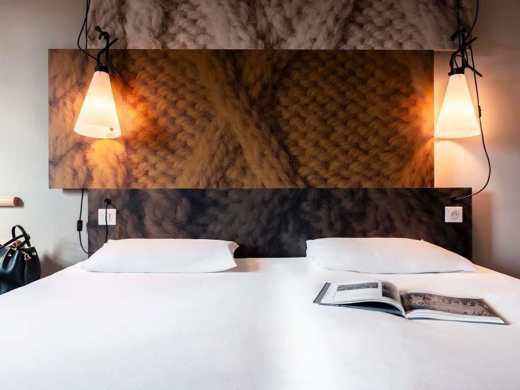 A hotel room with a bed, two bedside lamps, and a book on the bed.