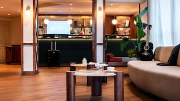 Een moderne hotellobby met een receptiebalie, een zithoek met een bank en een salontafel, en een grote plant.
