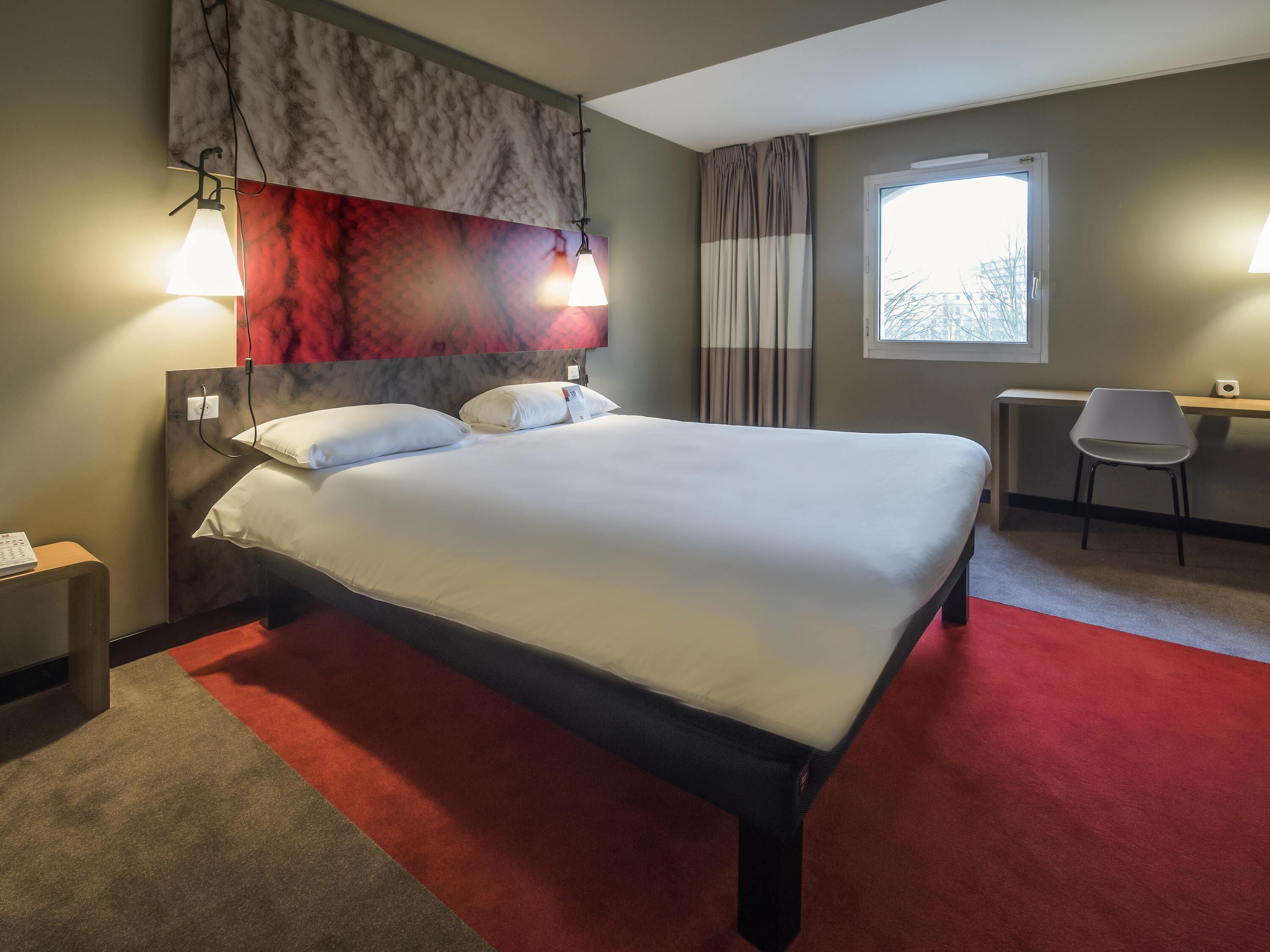 Una habitación de hotel con cama, lámparas de noche, escritorio, silla y ventana.