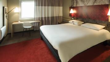 Habitación de hotel con cama, escritorio, silla y dos lámparas fijadas a la pared.