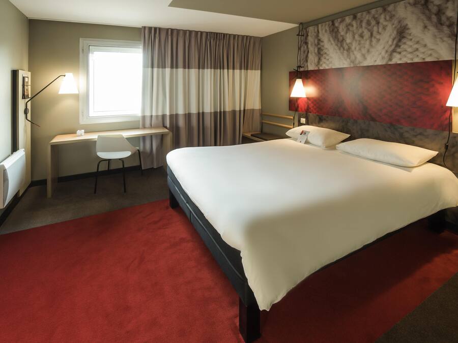 Habitación de hotel con cama, escritorio, silla y dos lámparas fijadas a la pared.