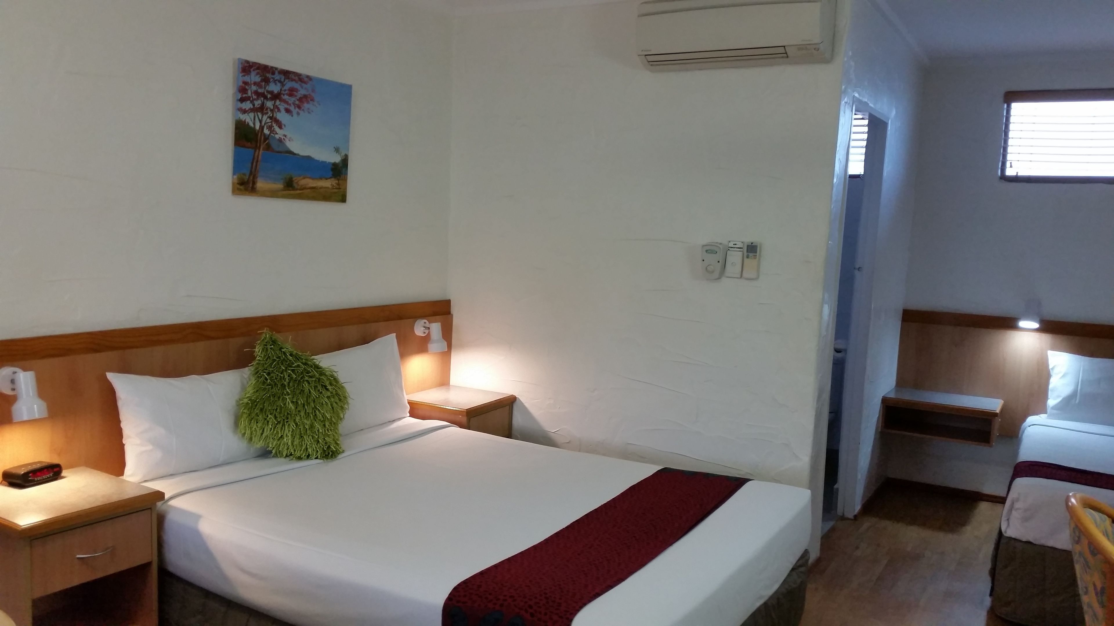 Habitación de hotel con cama, mesitas de noche, aire acondicionado de pared, un cuadro y una ventana.