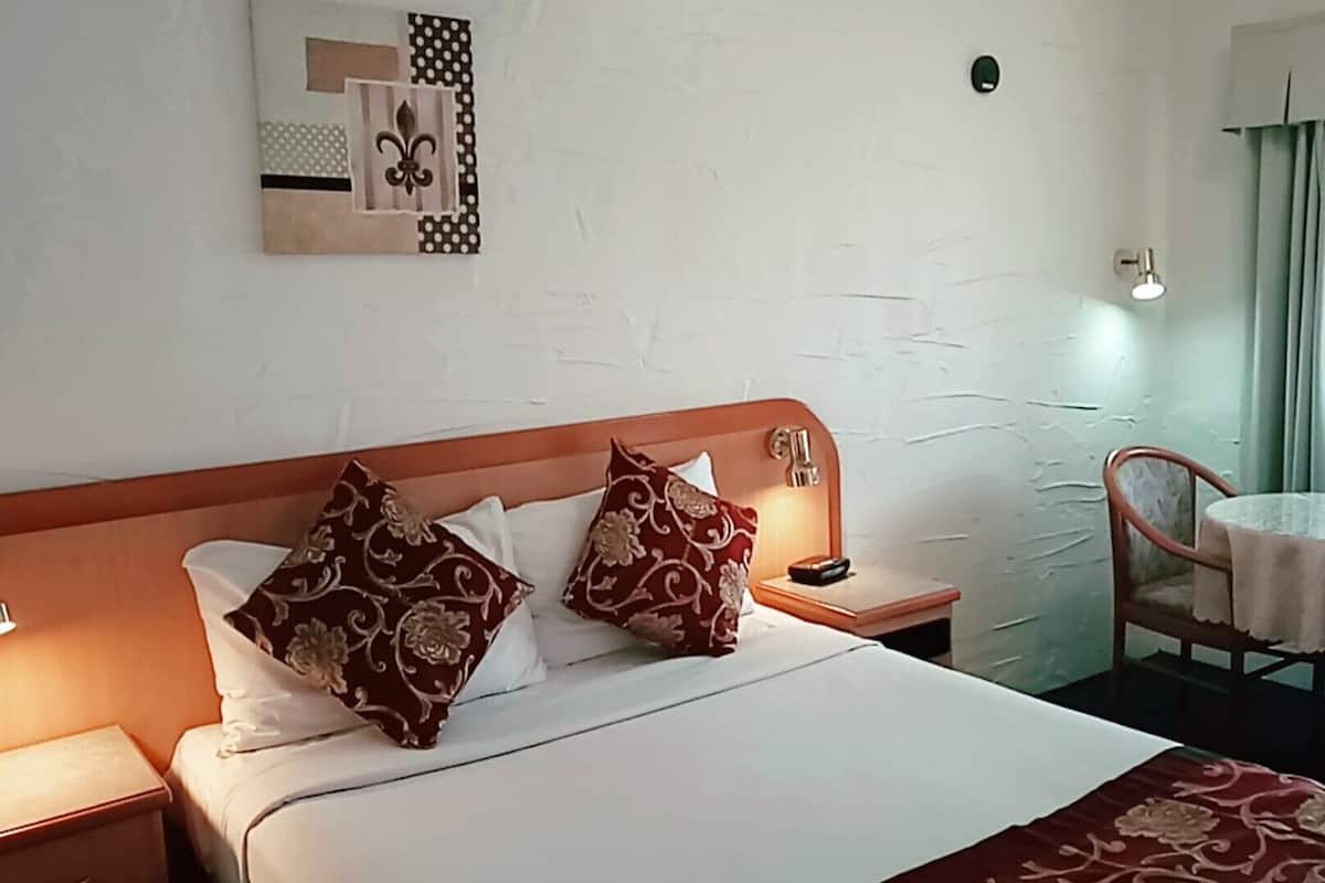 Ein Hotelzimmer mit einem Bett, zwei Nachttischen, einem Sessel und einem kleinen Tisch mit einer Lampe.