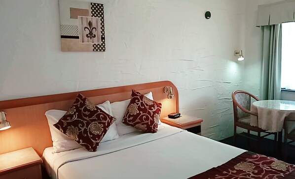 Una habitación de hotel con una cama, dos mesitas de noche, una silla y una pequeña mesa con una lámpara.