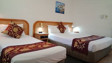A hotel room with two beds, each with a wooden headboard and bedside tables. There is a painting on the wall above the beds.