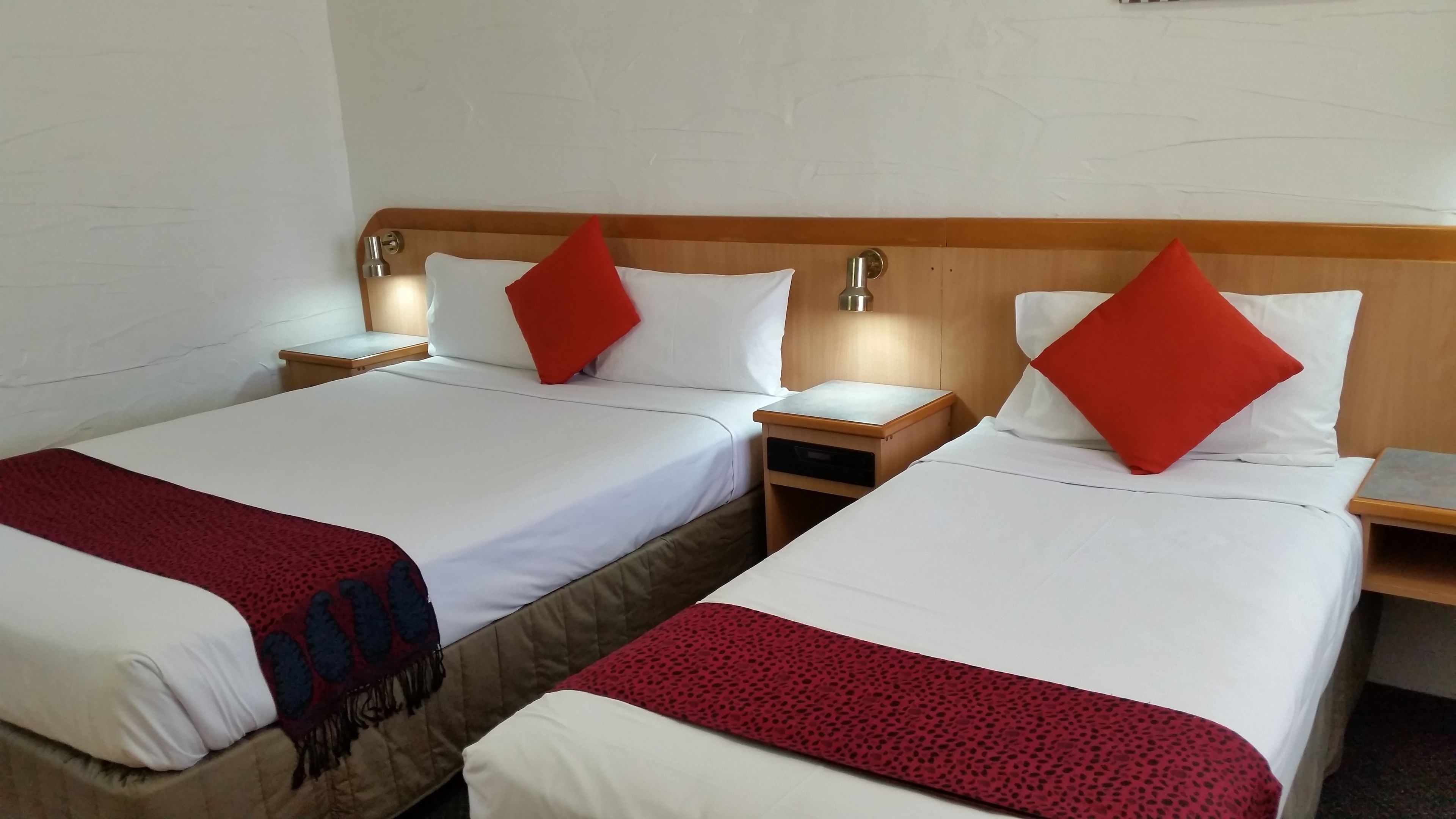 Two single beds with wooden headboards, white bedding, and red pillows. Each bed has a bedside table with a lamp.