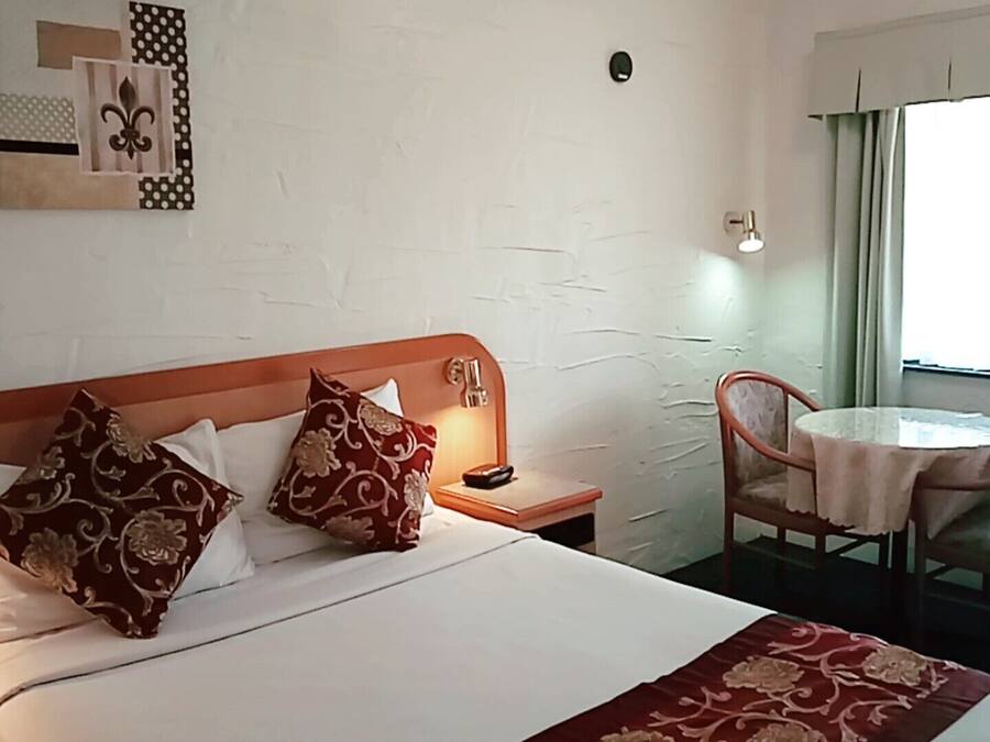 Una habitación de hotel con una cama, almohadas, una mesita de noche, una mesa y una silla.