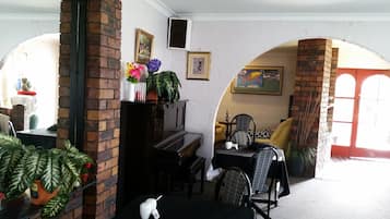 Una habitación acogedora con un piano, una mesa de comedor con sillas, una planta y un cuadro en la pared.