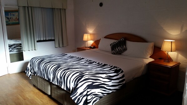 Habitación de hotel con edredón estampado de cebra, dos lámparas de noche, cabecera de madera y una ventana con cortinas.