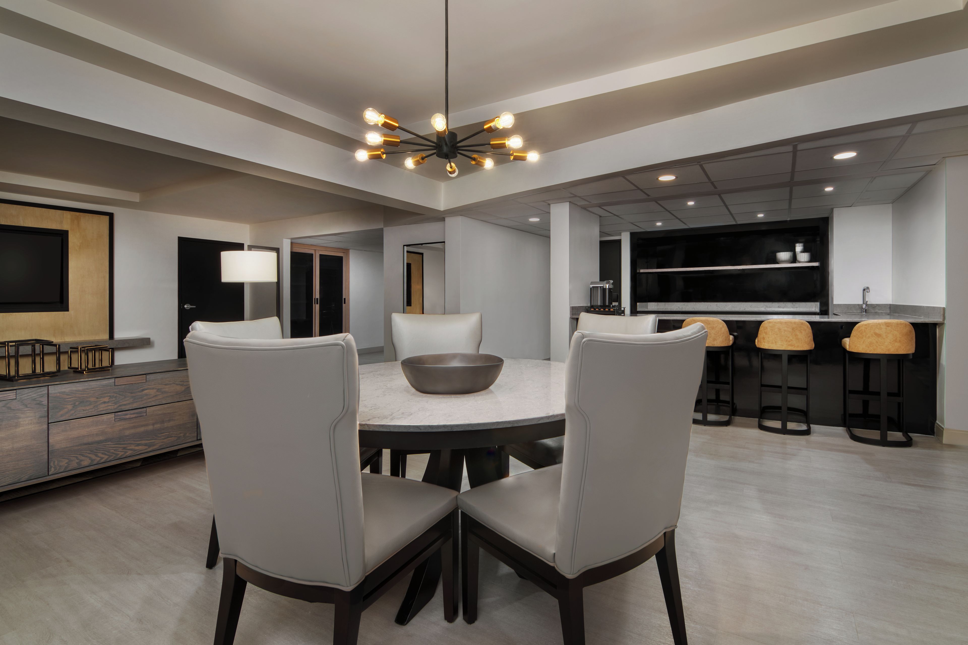 A modern dining area with a round table, four chairs, and a central light fixture.