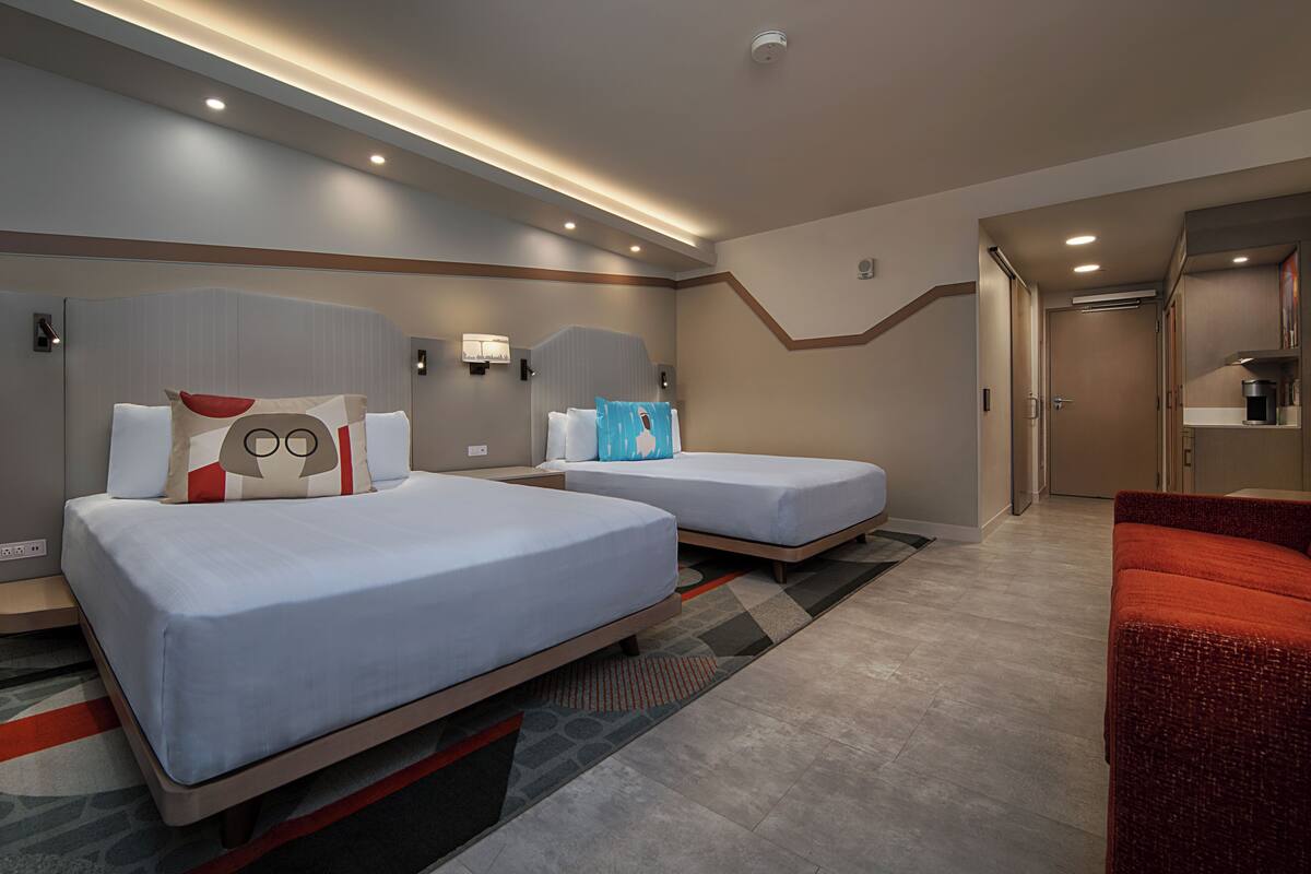 Une chambre d’hôtel avec deux lits, un canapé rouge et une kitchenette.