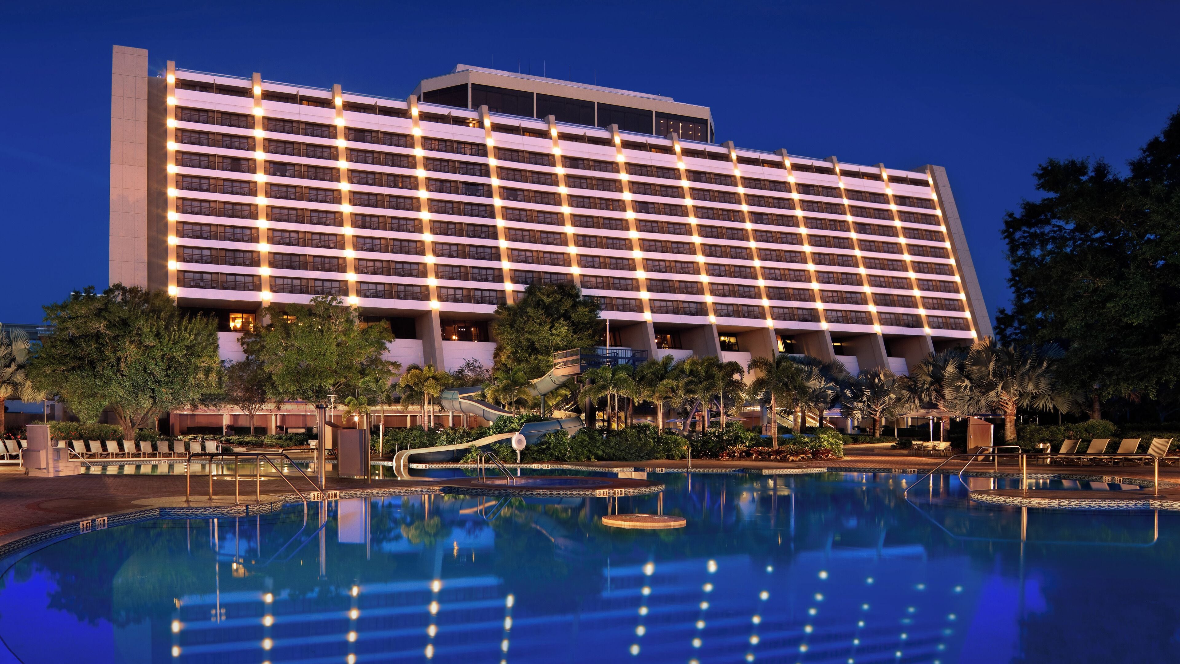 A large hotel with a pool area, including a water slide and lounge chairs.