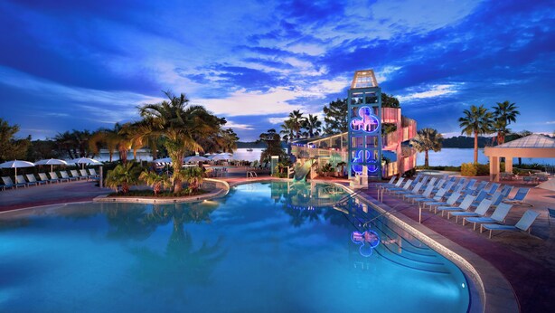 Un espace piscine avec des chaises longues, un toboggan aquatique et un bâtiment doté d’une enseigne lumineuse.