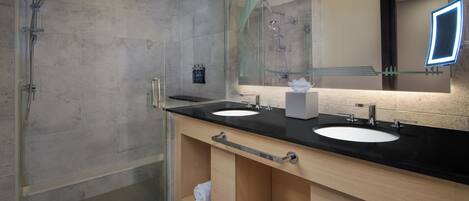 A modern bathroom with two sinks, a glass shower enclosure, and a large mirror with a lighted frame.