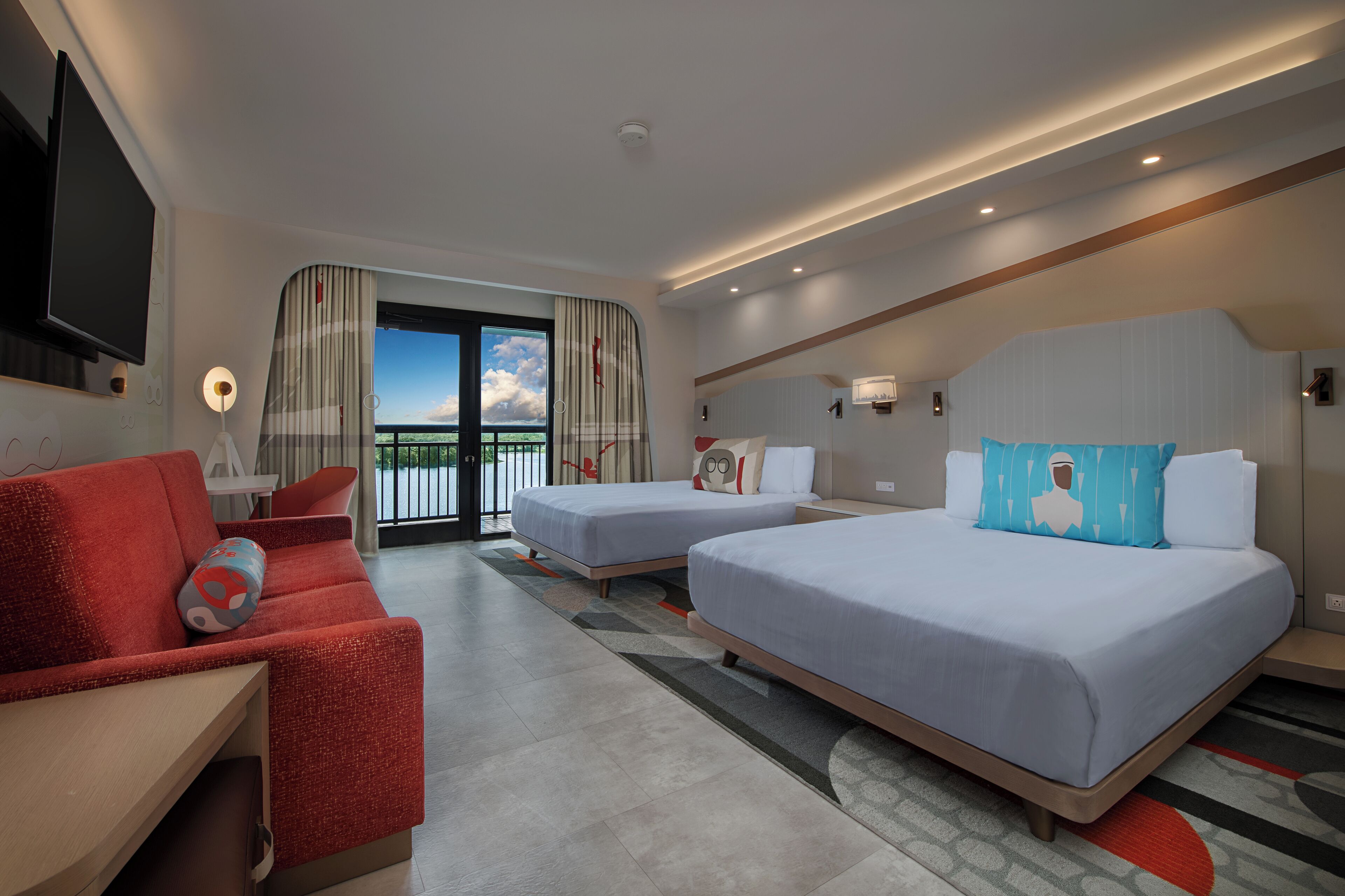 A hotel room with two beds, a red sofa, a TV, and a balcony with a view.