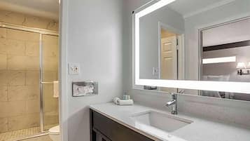 A modern bathroom with a glass shower enclosure, a large mirror, and a vanity with a sink.