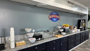 Zona de desayuno tipo bufé con un letrero que dice 'Baymont Breakfast Corner', diversas opciones de comida y una máquina de café.