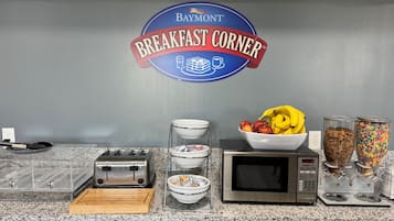 Una encimera de cocina con un tostador, microondas, cuencos y un frutero.