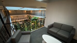 Un balcón amplio con un sofá gris, una mesa blanca y vistas a un exuberante jardín interior.