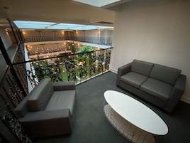 Un balcón amplio con un sofá gris, una mesa blanca y vistas a un exuberante jardín interior.