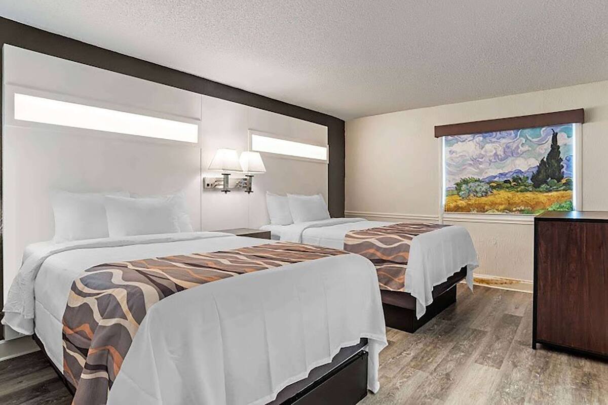 A hotel room with two beds, a painting on the wall, and a desk.