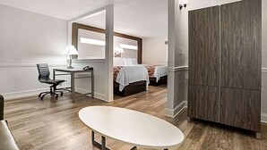 Habitación de hotel con escritorio, silla, dos camas, armario y un espejo grande.