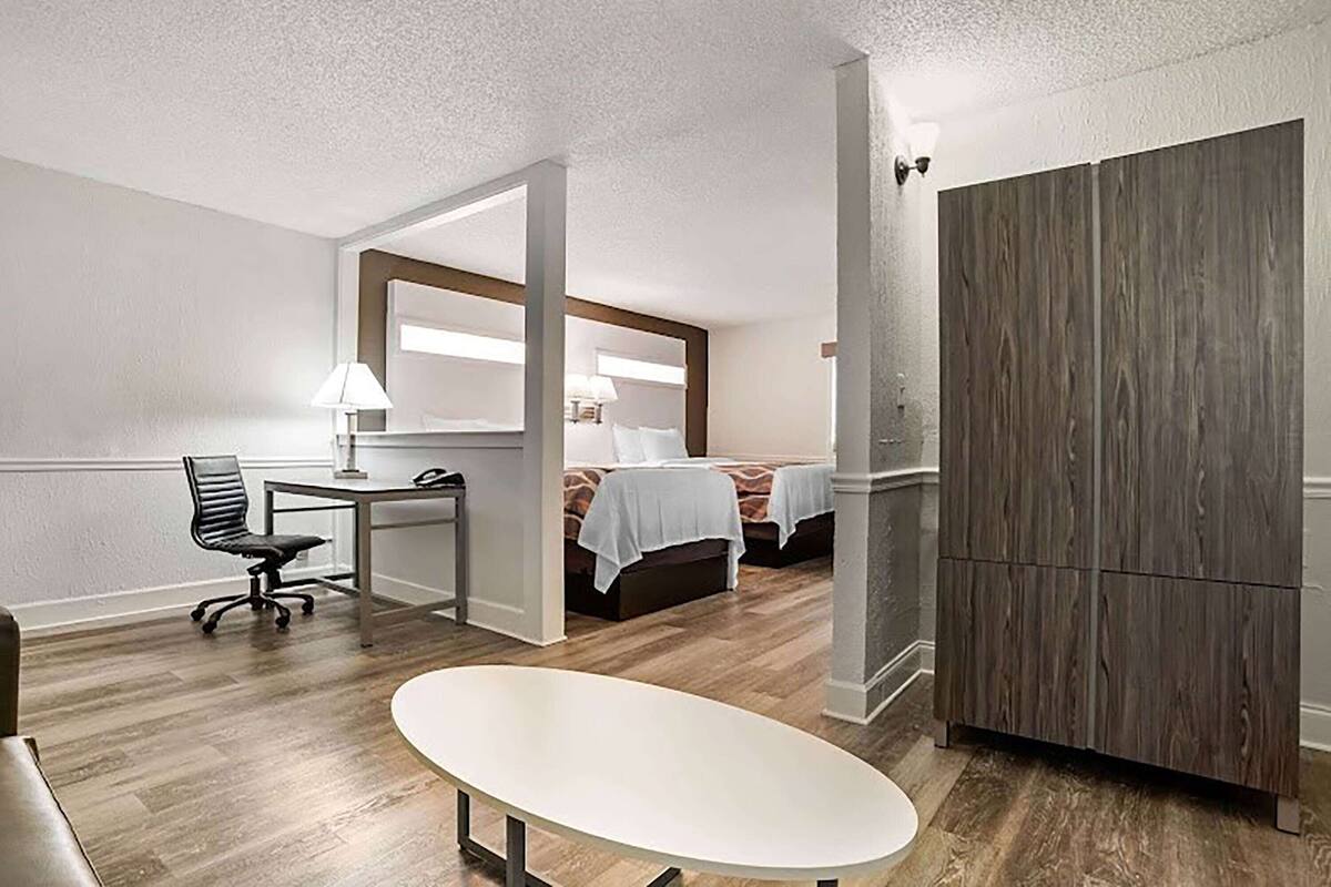 A hotel room with a desk, chair, two beds, a wardrobe, and a large mirror.