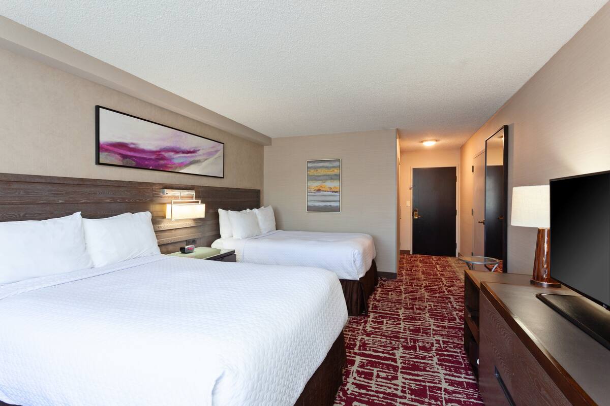 A hotel room with two beds, a TV, a desk, and a red carpet.