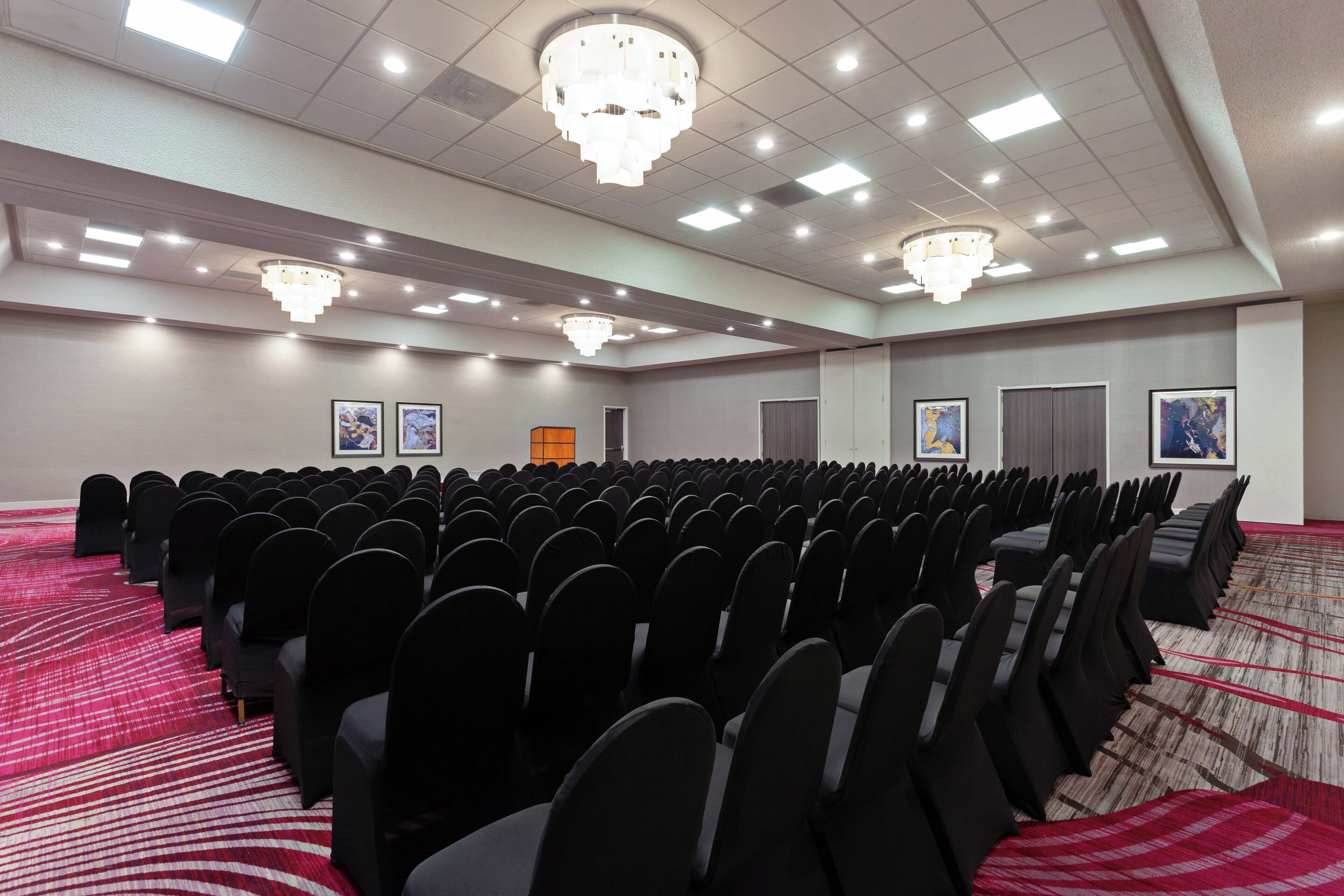 A conference room with rows of chairs, a carpeted floor, and ceiling lights.