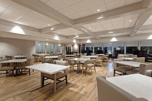 Een ruime, overdekte eetruimte met meerdere tafels en stoelen, een hoge plafond met ingebouwde verlichting en grote ramen voor natuurlijk licht.