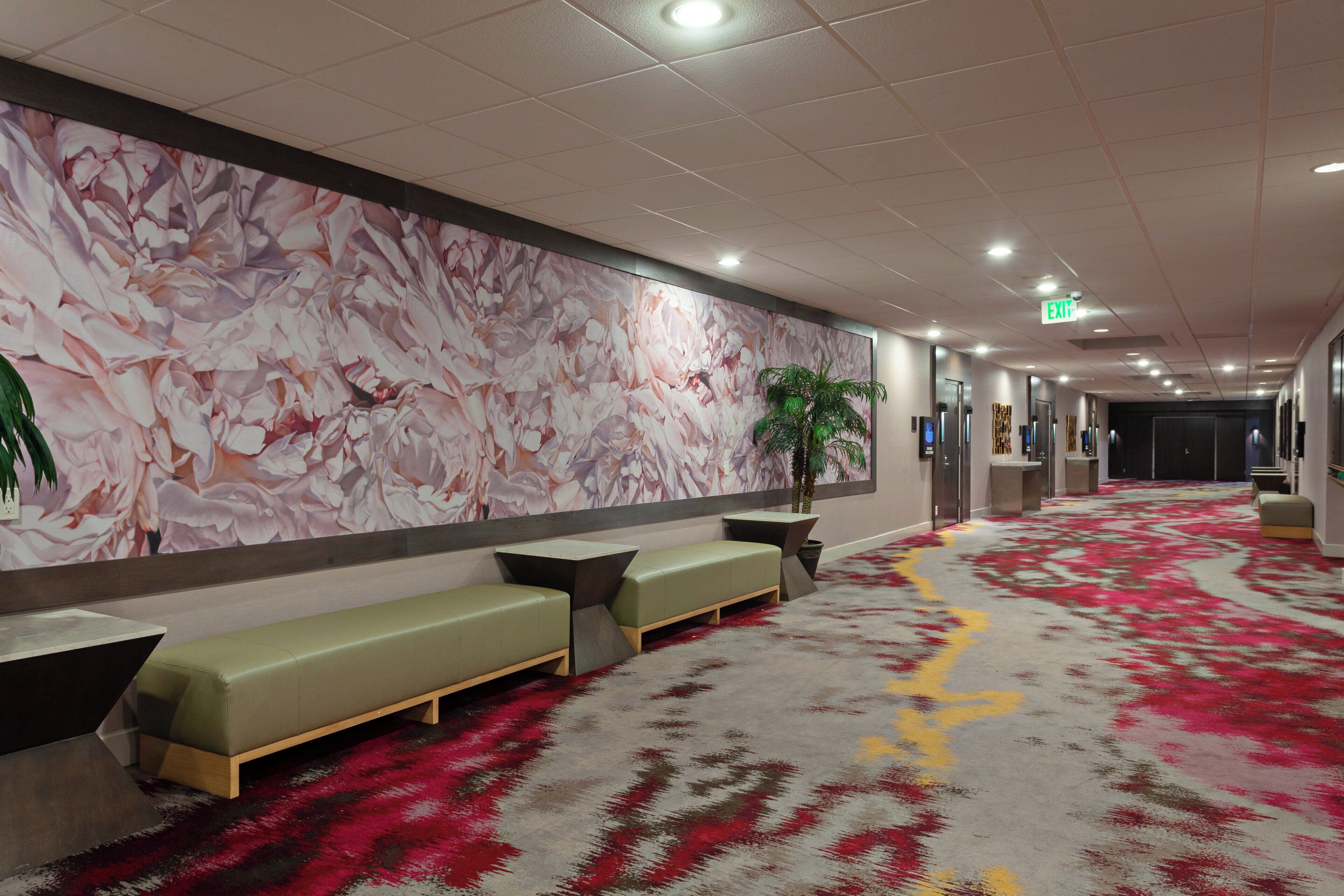 Un vestíbulo de hotel con un mural floral, zona de estar y suelo alfombrado.