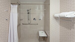 Un área de ducha con puerta de cristal, un perchero y una pequeña mesa con una toalla.