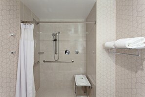 Un área de ducha con puerta de cristal, un perchero y una pequeña mesa con una toalla.
