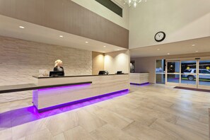 A reception area with a wooden reception desk, a clock on the wall, and a view of the street through the glass door. - Crowne Plaza Silicon Valley N - Union City by IHG (Union City)