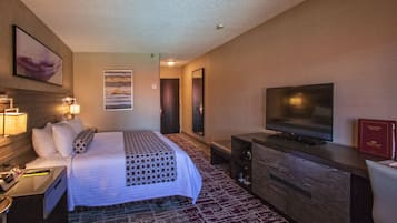 A hotel room with a bed, a television, a desk with a lamp, and a dresser.