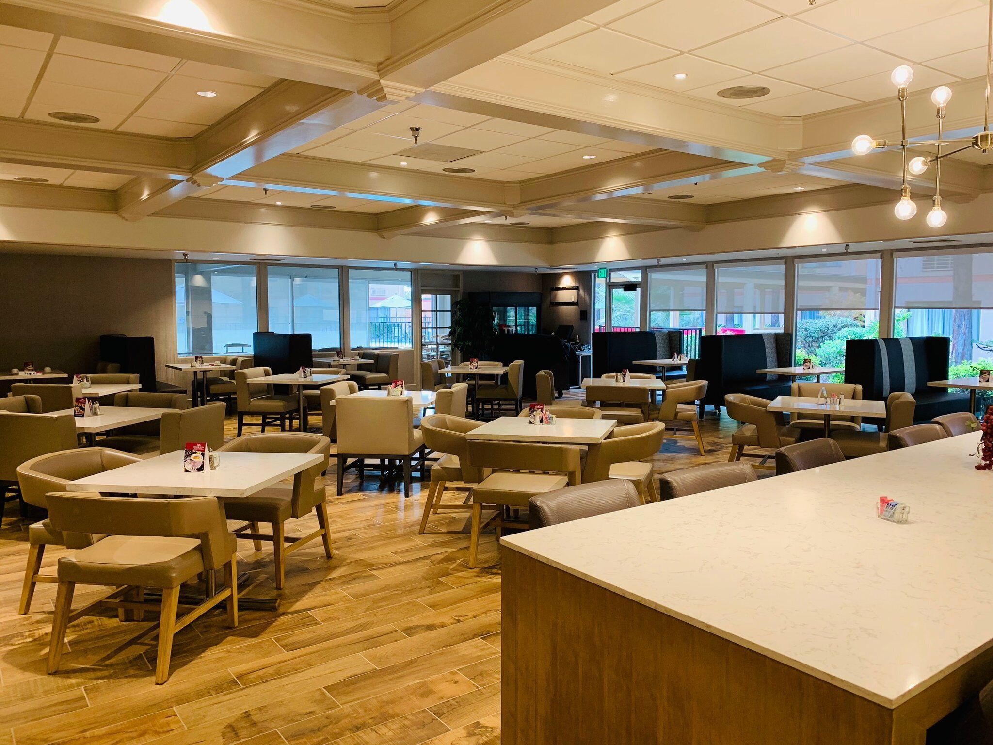 A spacious indoor dining area with multiple tables and chairs, large windows, and a modern ceiling design.