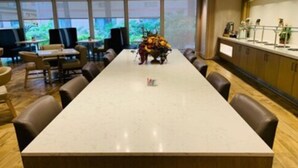 Una larga mesa de conferencias con sillas, un jarrón de flores y una zona de bar con mostrador y taburetes.