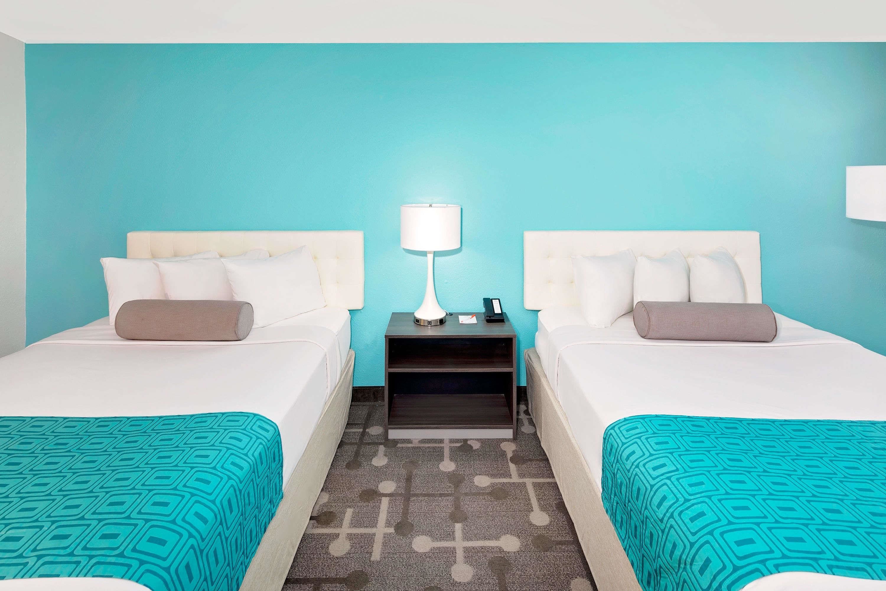 A hotel room with two beds, a nightstand with a lamp, and a patterned rug.