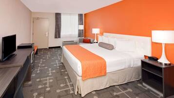 A hotel room with a bed, bedside tables, a desk with a TV, and a window with curtains.
