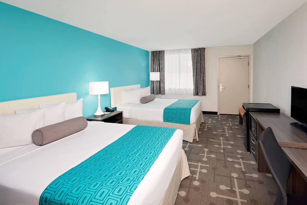 A hotel room with two beds, a desk, a TV, and a door.