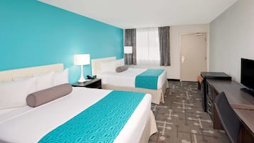 A hotel room with two beds, a desk, a TV, and a door.