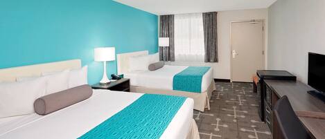 A hotel room with two beds, a desk, a TV, and a door.