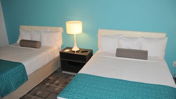 Two single beds with white headboards and teal-patterned bedspreads, a nightstand with a lamp, and a blue wall.