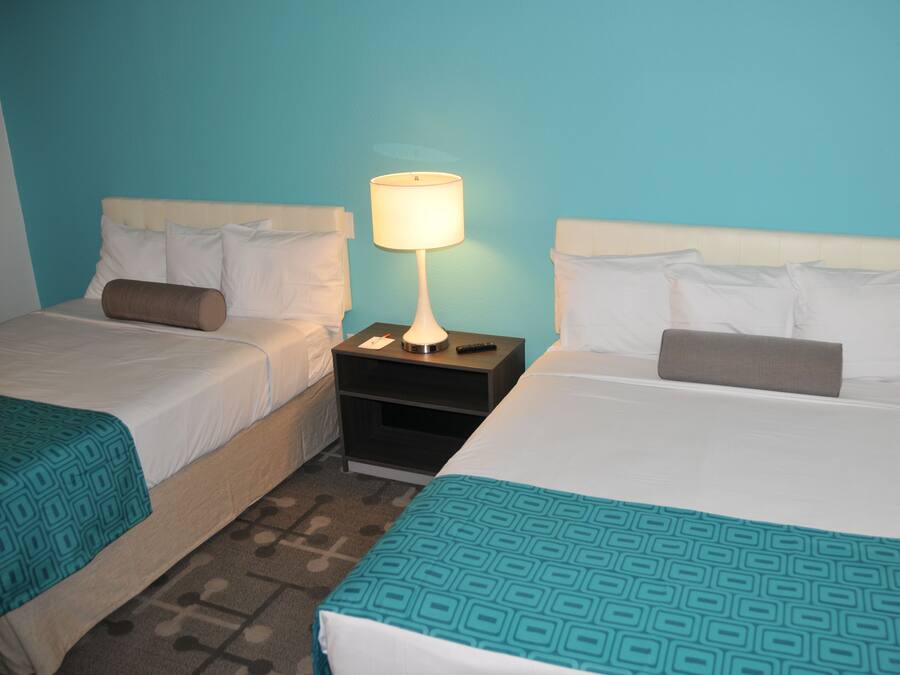 Two single beds with white headboards and teal-patterned bedspreads, a nightstand with a lamp, and a blue wall.