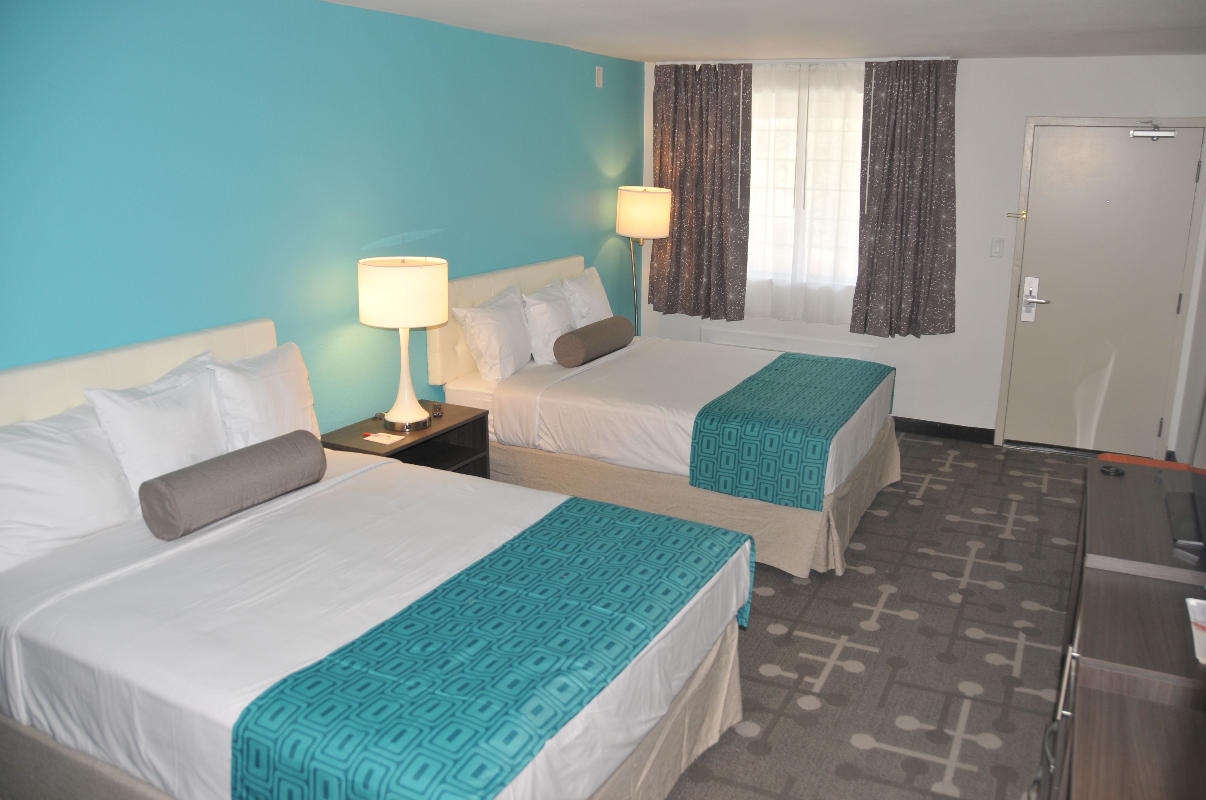 A hotel room with two beds, a desk, a lamp, and a window with curtains.