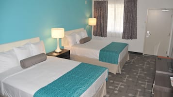 Habitación de hotel con dos camas, un escritorio, una lámpara y una ventana con cortinas.