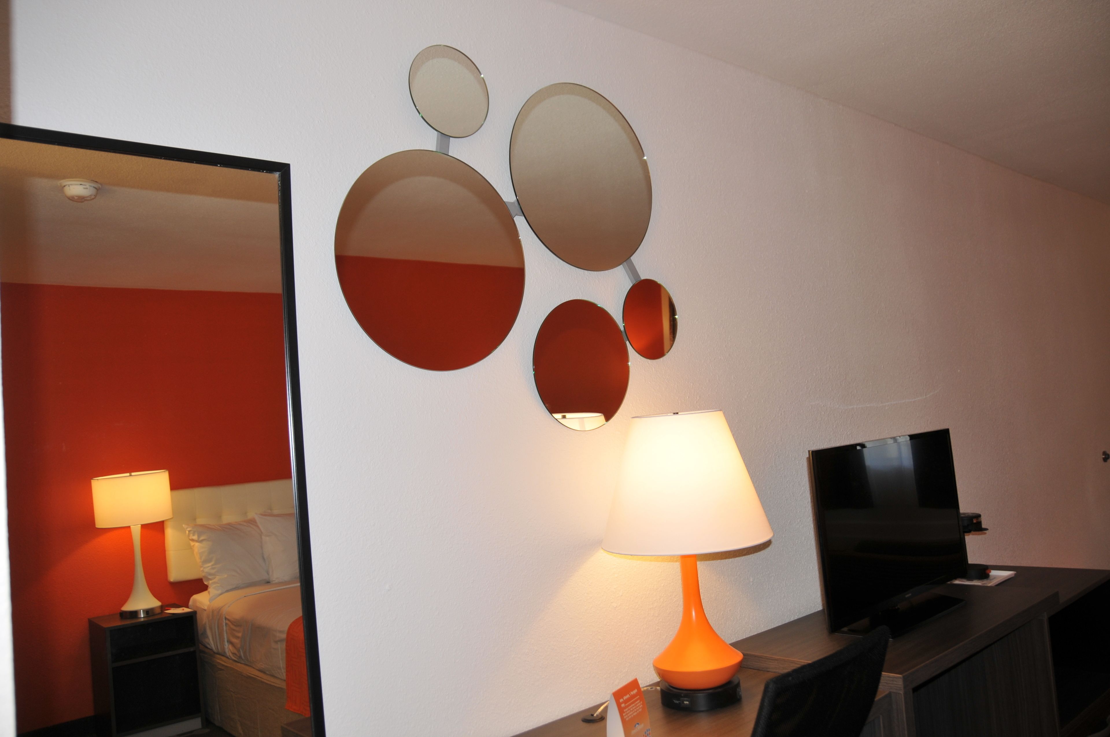 A hotel room with a bed, a nightstand with a lamp, a TV, and wall-mounted mirrors.