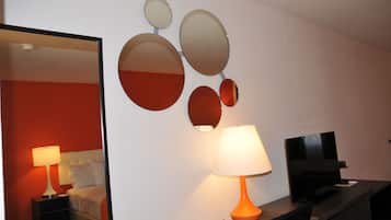 A hotel room with a bed, a nightstand with a lamp, a TV, and wall-mounted mirrors.
